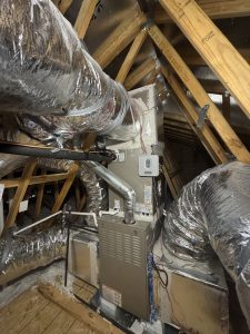 Indoor HVAC furnace and coil installed in an attic with surrounding ductwork and connections.